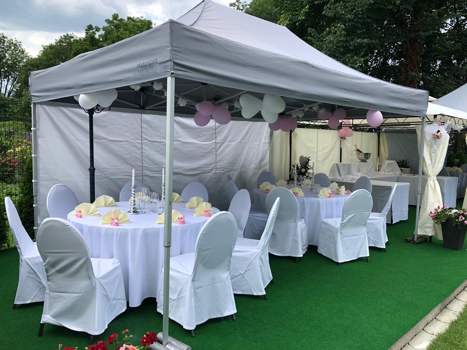Graues Faltzelt im Garten mit runden Tischen, weißen Sesselhussen und Luftballons